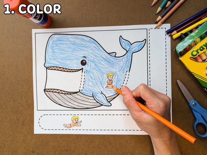 May include: A coloring page featuring a blue whale with a small figure inside. The whale is partially colored with blue, and an orange pencil is coloring the figure. Crayons, scissors, and glue are also visible.
