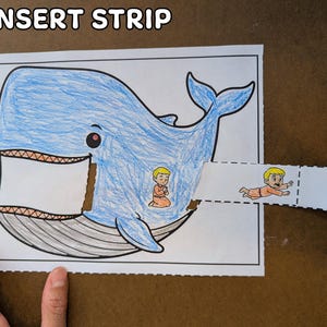 May include: A blue whale coloring page with a cut-out section for inserting a strip. The strip features a cartoon figure. The text "5. INSERT STRIP" is at the top.