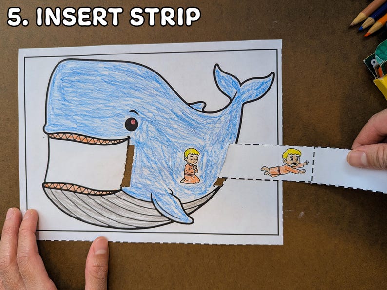 May include: A blue whale coloring page with a cut-out section for inserting a strip. The strip features a cartoon figure. The text "5. INSERT STRIP" is at the top.