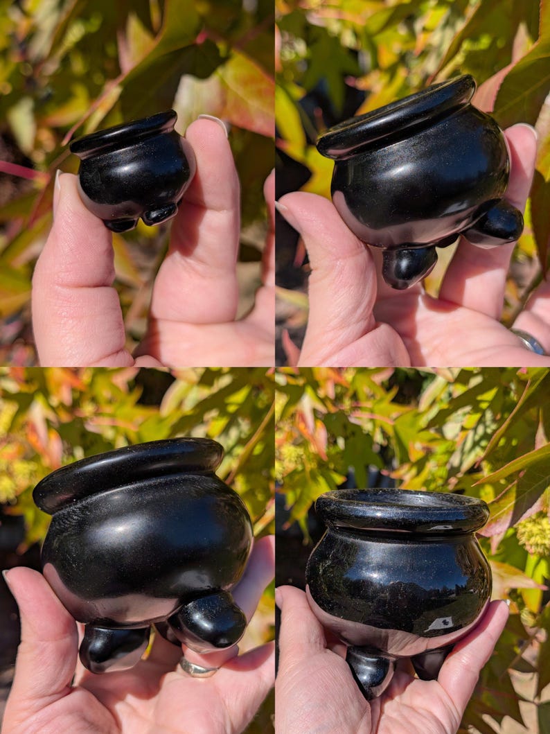 Pu&ograve; includere: Un piccolo oggetto nero lucido a forma di calderone, con tre piedini arrotondati e un bordo svasato. Il piccolo vaso ha una superficie liscia e riflettente, probabilmente realizzata in pietra lucida o materiale simile. L'oggetto &egrave; tenuto in una mano.