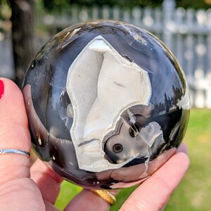 May include: A polished, spherical geode with a striking contrast of black and white patterns. The geode's interior reveals a crystalline structure, creating a unique and eye-catching decorative object. The sphere is held in a hand, showcasing its size and detail.