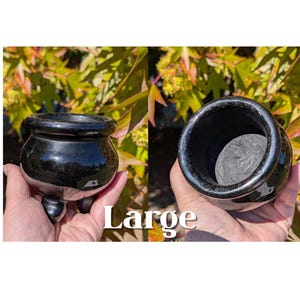 Pu&ograve; includere: Un vaso nero lucido, rotondo, a tre gambe con un bordo largo. Il vaso ha una superficie liscia e riflettente. La parola "Large" &egrave; stampata in bianco sull'immagine. Il vaso &egrave; tenuto in mano da una persona.