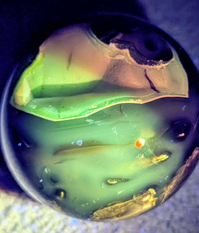 May include: A close-up of a translucent, spherical object with layers of green, yellow, and brown hues. The object has a smooth, polished appearance with internal structures visible. The lighting creates a glowing effect, highlighting the colors and textures.