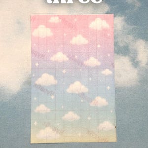 Puede incluir: Una pegatina rectangular con un dise&ntilde;o de cielo degradado, con nubes y estrellas. La pegatina tiene un patr&oacute;n de cuadr&iacute;cula y la palabra "three" en letras blancas en la parte superior. El fondo es un cielo azul claro lleno de nubes.