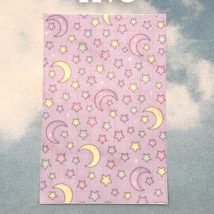 Puede incluir: Un trozo de papel rectangular con un patr&oacute;n repetitivo de estrellas amarillas y lunas crecientes en tonos de morado, rosa y verde sobre un fondo lavanda. La palabra "five" est&aacute; escrita en blanco en la parte superior.