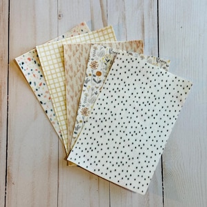 Könnte beinhalten: Eine Sammlung von Papierbögen mit verschiedenen Mustern, darunter Terrazzo, Gitter, Blumen und Punkte. Die Farbpalette umfasst Beige-, Creme- und gedämpfte Töne, die eine kohärente Ästhetik schaffen. Die Blätter sind fächerförmig angeordnet.