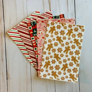 Op de afbeelding: Een waaier van zes vellen met kerstthema. Ontwerpen zijn onder meer rood-witte zuurstokstrepen, een rood-groen kerstboompatroon, een roze gespikkeld patroon en een wit vel met peperkoekmannetjes en sneeuwvlokken.