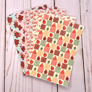 Könnte beinhalten: Vier Blätter Papier mit weihnachtlichen Mustern. Ein Blatt zeigt Lebkuchenmänner auf hellblauem Hintergrund. Ein anderes hat rote Schleifen auf rosa Hintergrund. Das dritte hat ein kariertes Muster mit Äpfeln und Lebkuchenmännern.