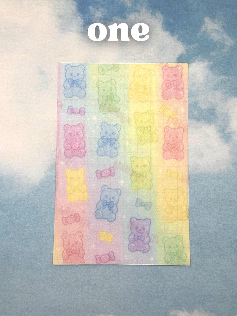 Puede incluir: Una hoja de pegatinas con un fondo degradado de arco&iacute;ris. Las pegatinas presentan ositos de peluche brillantes en varios colores, cada uno con una pajarita. La palabra "one" est&aacute; escrita en blanco en la parte superior.