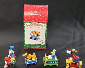 May include: A collection of Hallmark Merry Miniatures featuring Disney characters. The set includes Pluto's Coal Car and other figurines. The box is red with the Hallmark logo. The figurines are on a black surface.