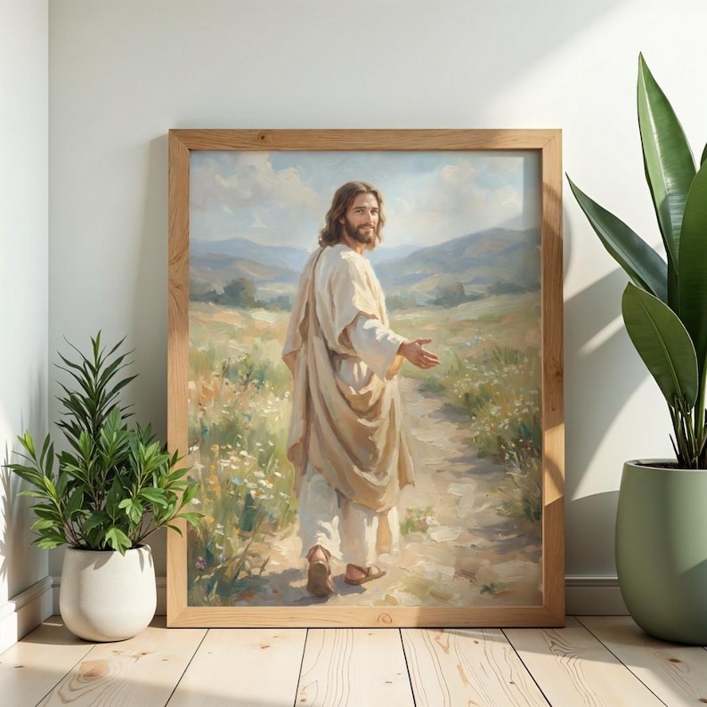 May include: A framed print of a person in a cream-colored robe walking on a path, looking back over their shoulder. The artwork is set in a landscape with a light brown wooden frame. The background features rolling hills and a bright sky.