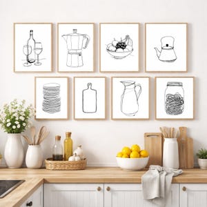 May include: A collection of eight framed black and white line art prints depicting kitchen and dining items. The prints include a wine bottle and glasses, a coffee maker, a bowl of fruit, a teapot, a stack of plates, a cutting board, a pitcher, and a jar.