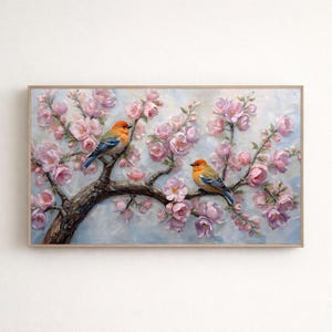 Puede incluir: Pintura enmarcada que representa dos pájaros posados en una rama de árbol en flor. Los pájaros tienen la cabeza naranja, las alas azules y el cuerpo amarillo y marrón. El árbol tiene flores rosas sobre un fondo azul claro.