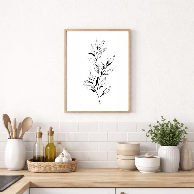 May include: A framed botanical art print featuring a black and white line drawing of leaves and stems. The artwork is displayed on a white wall above a kitchen countertop with various decorative items.