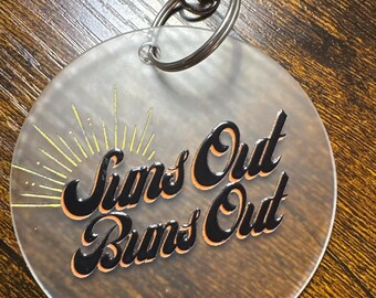 Brelok Suns Out Buns Out, 3" z matowego akrylu, okrągły, prezent dla nudystów z metalowym obrotowym haczykiem, zabawny, letni brelok na plażę