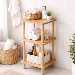 May include: A three-tiered wooden bathroom shelf unit with rolled white towels, baskets, and toiletries. The shelves are made of light-colored wood, and the unit has a simple, modern design. The baskets are woven, and the toiletries include bottles and a soap dispenser.