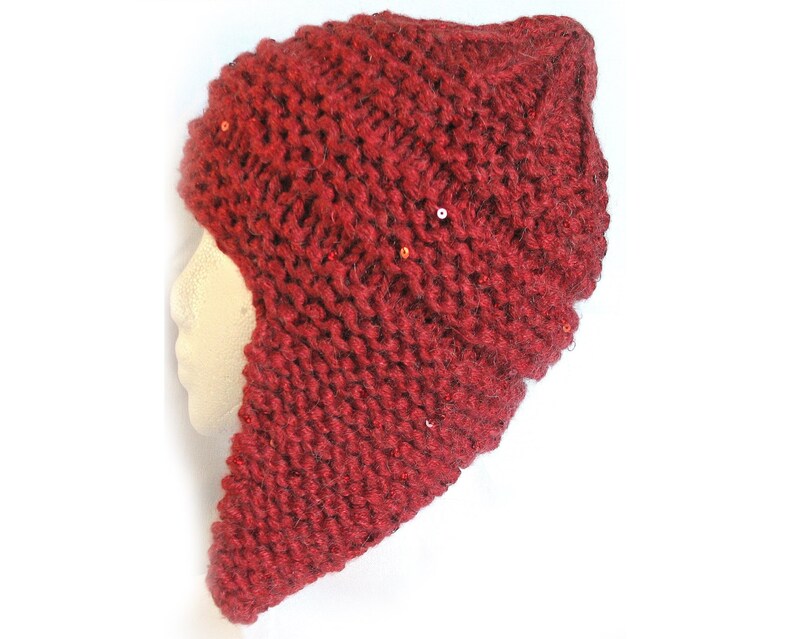 以下が含まれることがあります： 耳と首を覆う長いフラップが付いた赤いニット帽。帽子は質感のあるニットで、小さなスパンコールで飾られています。