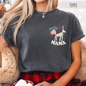 May include: Dark gray t-shirt with a graphic of a Dalmatian dog wearing a party hat and holding balloons. The text "pawty mama" is above the dog and "MAMA" is below. The shirt has rolled-up sleeves.