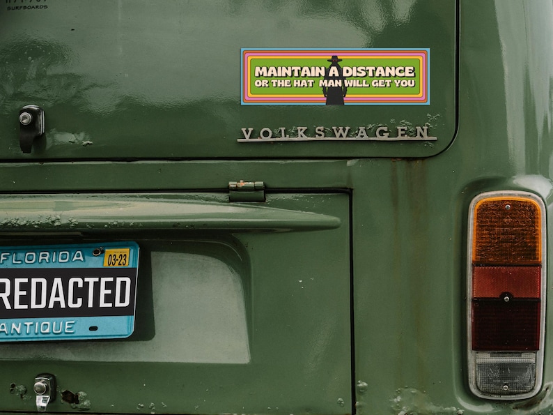 The back of a vintage Volkswagen with the bumper magnet on it. The license plate number is blacked out and says "redacted."