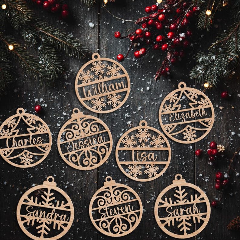 May include: Wooden Christmas ornaments with personalized names, including "William," "Elizabeth," and "Charles." Each ornament features a unique design with snowflakes and a tree. The ornaments are displayed on a dark wooden surface with festive decorations.