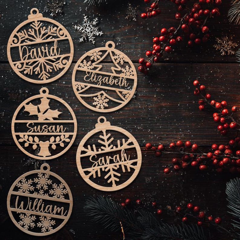 May include: Wooden Christmas ornaments with names David, Elizabeth, Susan, Sarah, and William. Each ornament is circular with a decorative cutout design, including snowflakes, a tree, and holly. The ornaments are made of light-colored wood.