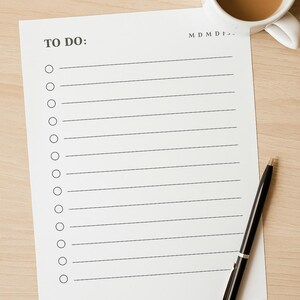 May include: A white to-do list with lines and circles, the words "TO DO:" at the top. A black pen rests on the paper, and a white mug of coffee sits nearby on a light wood surface.