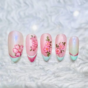 Uñas postizas Aura en tonos rosa y menta con flores de cerezo pintadas a mano.