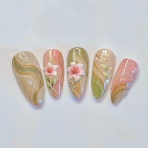 May include: A set of five almond-shaped press-on nails featuring a glossy finish with swirling sage green, beige, and gold accents. Two nails are adorned with raised 3D pink lily floral designs, while others feature delicate white pearl embellishments.