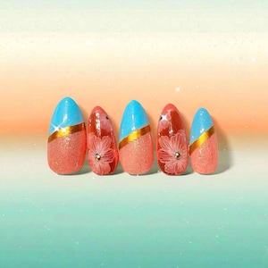 May include: A set of five artificial nails with a glittery peach base. Two nails have a light blue tip with a gold stripe, while the other three feature a floral design with a gold center. The nails are oval-shaped.