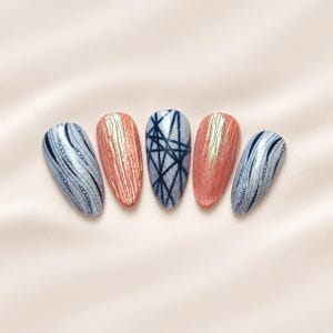 May include: Five almond-shaped press-on nails featuring varied designs. Two nails have silver glitter with black wavy lines and circles, two have a textured metallic copper finish, and the center nail has silver glitter with black crisscross lines.