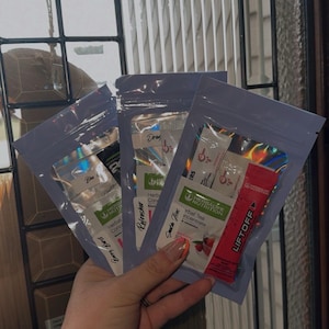May include: Three small, lavender-colored pouches filled with individual packets of Herbalife products. The packets are white, red, and black, with text including "Herbal Concentrate", "LiftOff", and "Berry Burst".