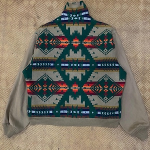 May include: A zip-up jacket featuring a tan base color with solid tan sleeves and a ribbed hem and cuffs. The back panel displays a prominent geometric pattern in shades of forest green, orange, red, white, and dark blue across the upper back.