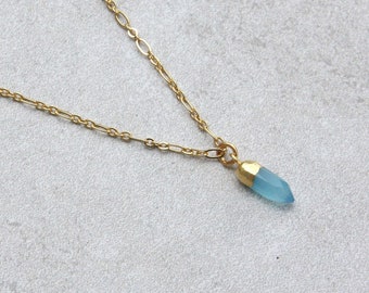 Könnte beinhalten: Eine zarte goldene Kettenkette mit einem hellblauen Edelstein-Anhänger. Der Anhänger ist in Form eines langen, dünnen Tropfens geformt.