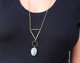 May include: A gold chain necklace with a geometric pendant featuring a triangle and a circle. The pendant is attached to a large, light blue gemstone.