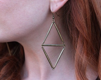 May include: A pair of geometric earrings made of gold-toned metal. The earrings are shaped like a diamond with a horizontal bar in the center.
