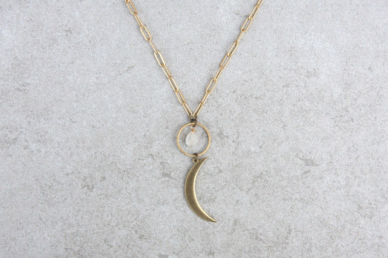 May include: A gold chain necklace with a crescent moon charm and a small clear crystal hanging from a circle.