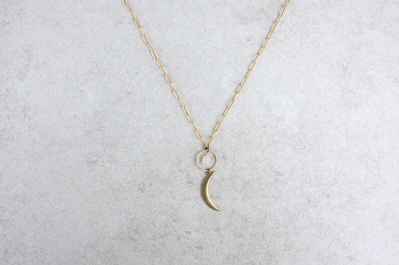 May include: A gold chain necklace with a crescent moon charm and a small clear crystal hanging from a circle.