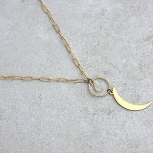 May include: A gold chain necklace with a crescent moon pendant and a small clear stone hanging from a circle.