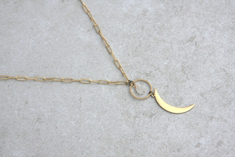May include: A gold chain necklace with a crescent moon pendant and a small clear stone hanging from a circle.
