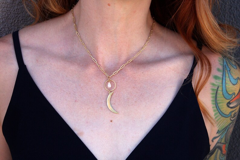 May include: A gold chain necklace with a crescent moon pendant and a small white stone in a circle.