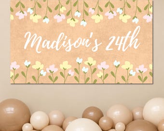 May include: A rectangular sign with a light tan background featuring white text that reads Madison's 24th. The top and bottom borders are decorated with a repeating pattern of small, simple flowers in shades of pale pink, yellow, and white.