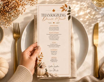 May include: A rectangular Thanksgiving dinner menu card featuring a cream background with autumn leaf illustrations and a small white pumpkin at the bottom. The text lists appetizers, main course, sides, desserts, and drinks in black and orange fonts.