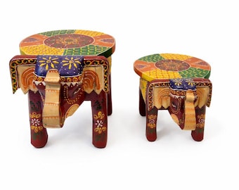 May include: Two decorative wooden elephant stools. The stools are painted with vibrant colors, including red, yellow, green, and purple. The elephant-shaped legs and round tops feature intricate floral patterns. The larger stool measures approximately 12 inches in height.