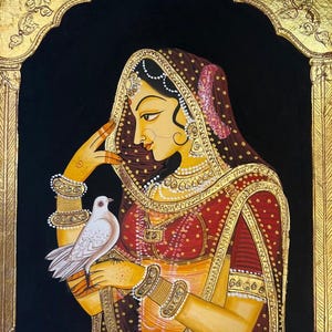 May include: An Indian miniature painting of a woman in traditional attire, holding a white dove. The artwork features intricate gold detailing, a black background, and a decorative archway. The woman wears a red and gold sari and jewelry.