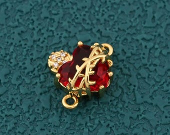 May include: A gold-colored charm with a red gemstone design, featuring the letter "A". The charm has a small loop for attaching to jewelry. A small cluster of clear stones is also present.