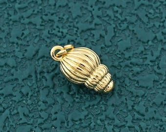 Puede incluir: Un pequeño dije dorado con forma de concha estilizada. El dije tiene un lazo en la parte superior para sujetarlo a una cadena o pulsera. El diseño de la concha presenta detalles acanalados y un acabado liso y pulido.