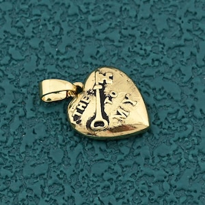 May include: A gold-colored heart-shaped pendant with the words "The Key to My" and a key design. The pendant has a small loop for a chain and is set against a textured teal background.