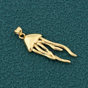 May include: A gold-colored pendant in the shape of a jellyfish. The pendant has a detailed design with a bell-shaped head and flowing tentacles. The pendant is suspended from a small loop at the top.