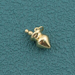 May include: A small, polished gold-tone metal charm shaped like a stylized gourd or pear. The charm features a smooth, reflective surface with a rounded body, a tapered neck, and a small circular loop at the top for attachment to a chain or cord.