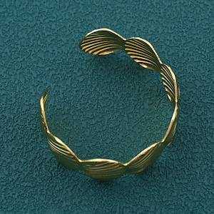 May include: A gold-colored cuff bracelet with a leaf-like design. The open-ended bracelet features a series of stylized, overlapping leaf shapes, creating a textured and organic aesthetic. The bracelet is made of a shiny, metallic material.